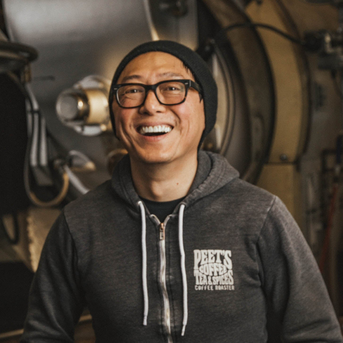 A peet's employee smiling while standing in front of a coffee roaster